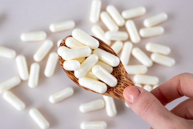 Capsules blanches de vitamine C dans une cuillère en bois sur fond beige avec des médicaments dispersés