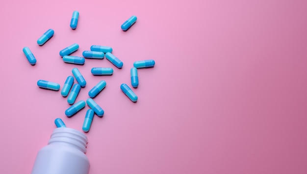 Capsules Bleues étalées Sur Une Bouteille De Médicament En Plastique Blanc Sur Fond Rose. Bannière De Pharmacie. Pharmacie En Ligne. Médicament Analgésique Et Concept De Résistance Aux Antibiotiques. Industrie Pharmaceutique.