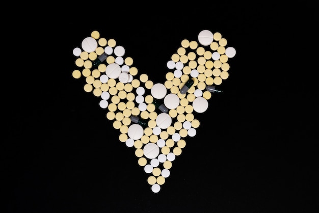 Capsules et comprimés de couleur blanche et jaune. Forme de coeur. Fond noir