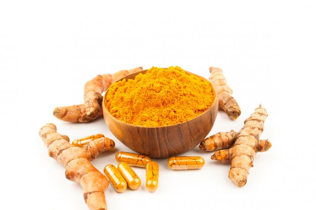 Capsules de curcuma et poudre de curcuma dans un bol en bois sur fond blanc. À base de plantes