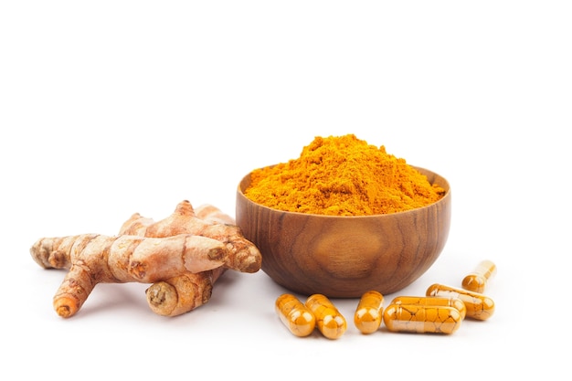 Capsules de curcuma et poudre de curcuma dans un bol en bois sur fond blanc.