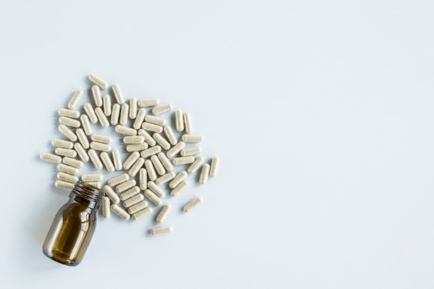 Capsules débordant de la bouteille de verre sur fond blanc