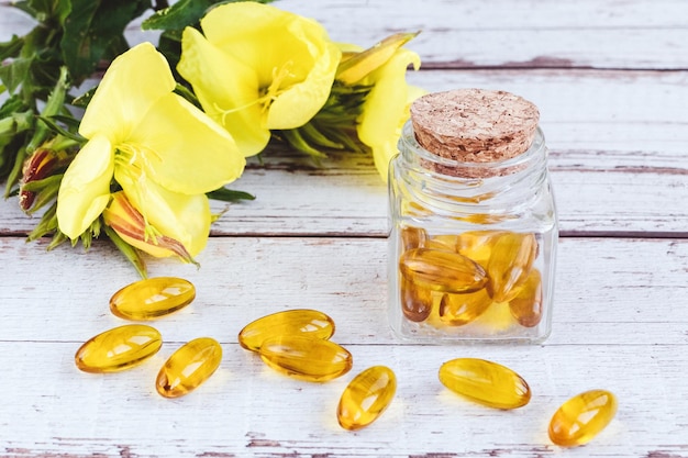 Capsules de gel d'huile d'onagre dans des pilules de bouteille en verre et des fleurs jaunes sur une table en bois