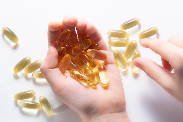 Capsules d'huile de foie de morue avec de la vitamine D dans la main de l'enfant sur fond blanc.