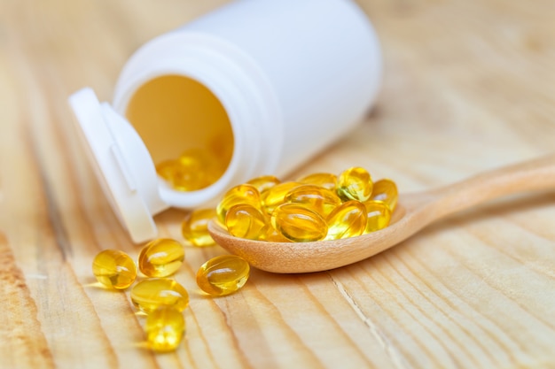 Capsules d&#39;huile de poisson avec oméga 3 et vitamine D sur bois de cuillère avec fond en bois