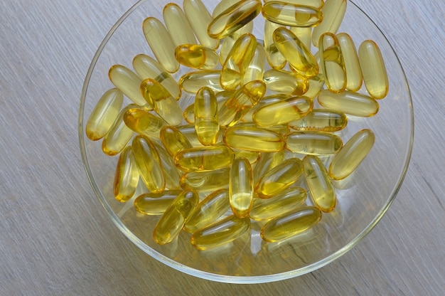 Capsules d'huile de poisson oméga-3 et vitamine D dans une assiette en verre.
