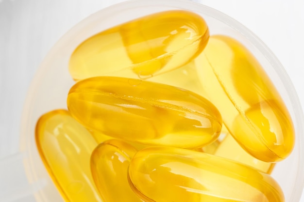 Capsules jaunes oméga-3 dans une cuillère en plastique, suppléments nutritionnels, gros plan, vue de dessus.