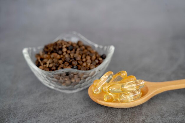 Photo capsules de poivre noir dans une cuillère en bois avec des granules de poivre noir dans un bol en verre