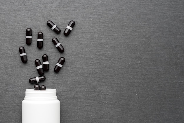 Des capsules de supplément noires sont versées à partir d'une bouteille blanche. Vue de dessus, mise à plat, espace de copie. Thème de la médecine, concept de soins de santé.