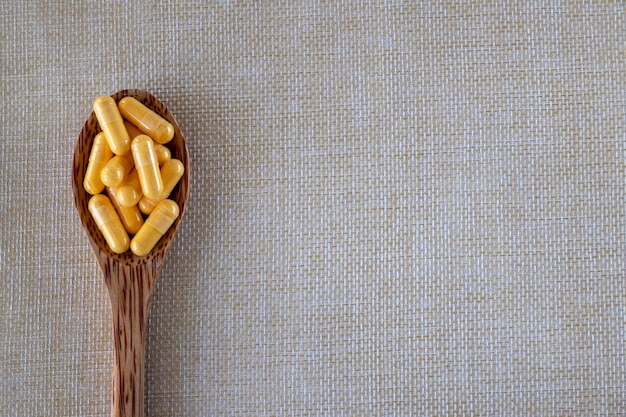 Capsules de vitamine Coenzyme Q10 dans une cuillère en bois sur fond beige Vue de dessus espace de copie