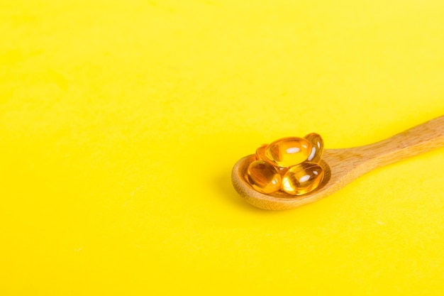 Capsules de vitamine oméga dans une cuillère sur un fond coloré Comprimés servis comme un repas sain Capsules de supplément de vitamines en gel souple rouge sur une cuillère