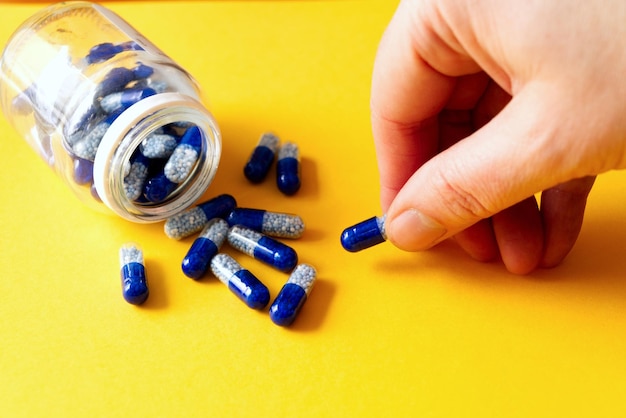 Photo des capsules de vitamines bleues renversées dans un pot sur un fond jaune