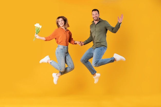 Photo capture complète d'un couple européen heureux sautant haut femme tenant un bouquet de fleurs fraîches homme et