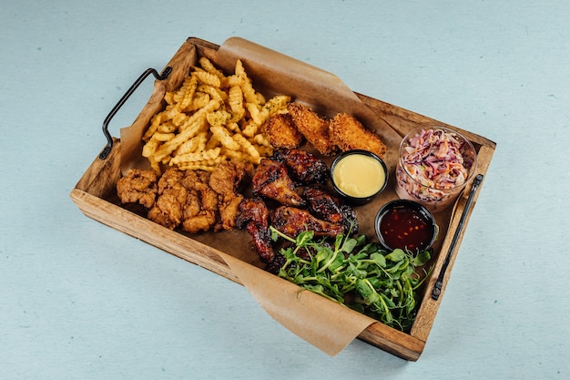 Photo capture en grand angle de poulet frit avec frites et sauce sur un plateau en bois sur la table