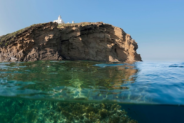 Capture horizontale d'une île avec un phare vue de la mer avec une partie de l'image sous l'eau