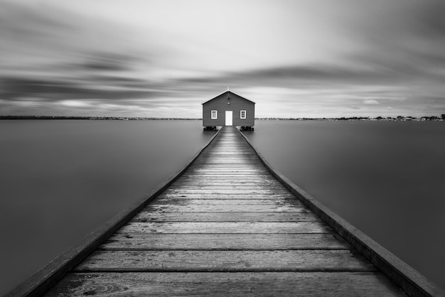 Capture en niveaux de gris d'une route en bois menant à une maison solitaire - concept de monde imaginaire