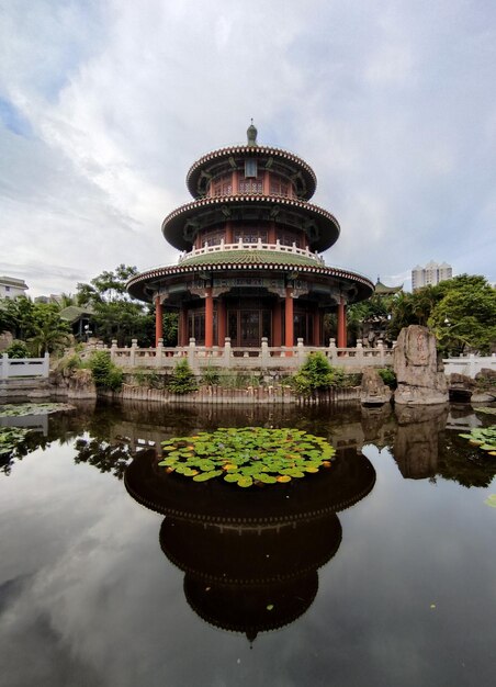 Capture verticale du tombeau de Hai Rui sous un ciel nuageux avec une réflexion sur l'eau de l'étang, Haikou, Hainan, Chine