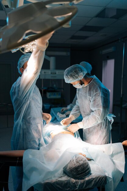 Photo capture verticale d'être opéré par des chirurgiens professionnels médecin masculin ajustant la lumière effectuant
