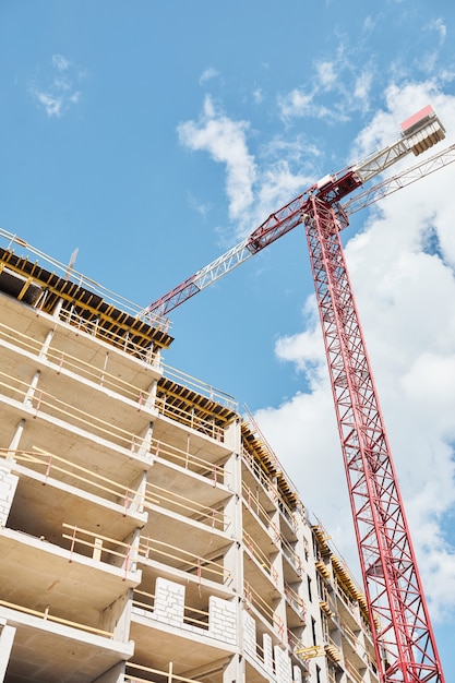 Capture verticale à faible angle de la construction d'une maison d'habitation d'une grue de construction contre le ciel bleu, espace pour copie