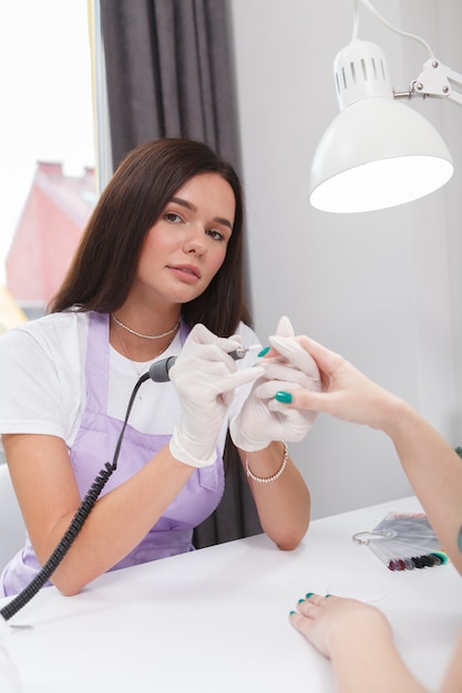 Capture verticale d'une manucure professionnelle regardant la caméra tout en faisant les ongles d'un client