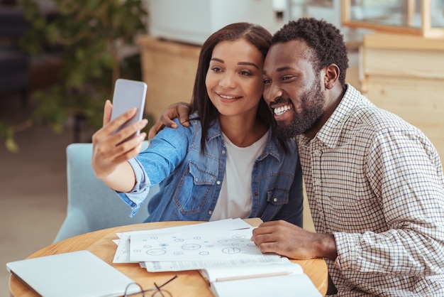 Capturer le moment. Collègues optimistes agréables assis dans le café, discutant de documents de travail et prenant une courte pause pour prendre un selfie ensemble