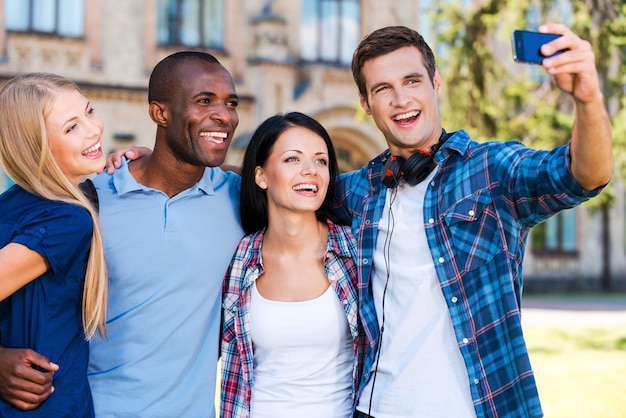 Capturer un moment de la vie étudiante. Quatre jeunes heureux faisant un selfie en se tenant près les uns des autres à l'extérieur