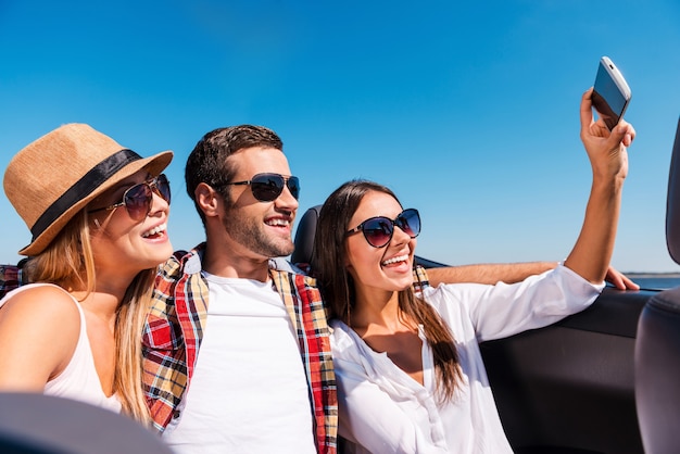 Capturer le plaisir. Trois jeunes heureux profitant d'un voyage en voiture décapotable et faisant du selfie