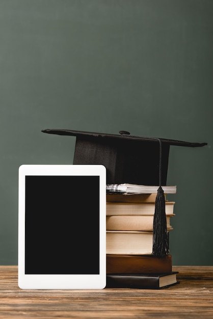 Capuchon académique de cahier de livres et tablette numérique avec écran blanc sur une surface en bois isolée sur