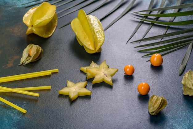 Carambole de fruits, accessoires de plage et feuillage d'une plante tropicale sur papier de couleur. étoiles de mer et fruits