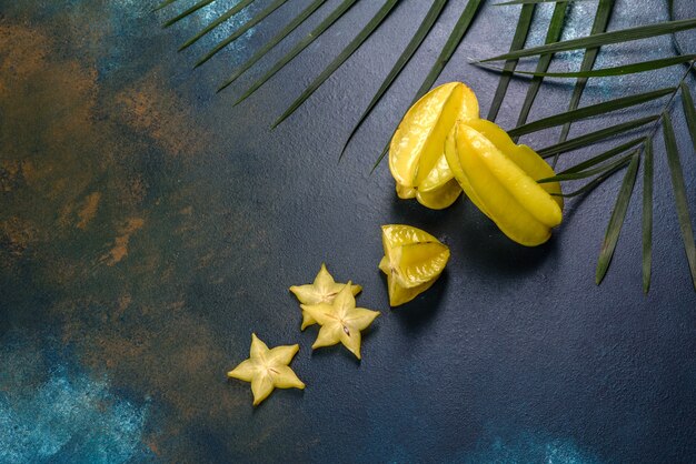 Carambole de fruits, accessoires de plage et feuillage d'une plante tropicale sur papier de couleur. Fond d'été avec des étoiles de mer et des fruits