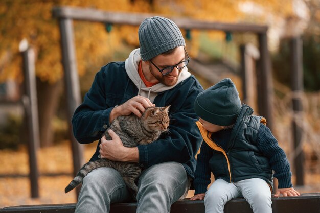 Photo caresser un chat le père et le jeune fils sont ensemble à l'extérieur pendant la journée