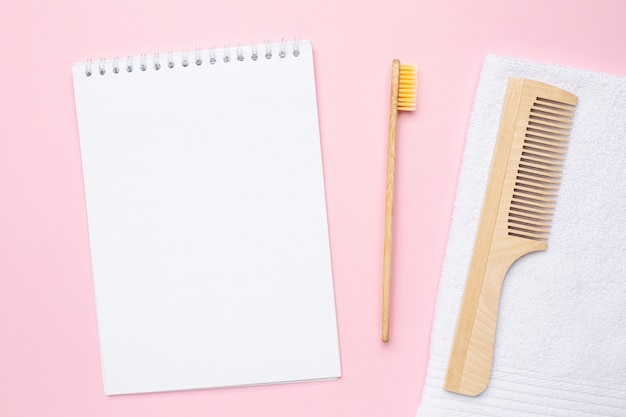 Carnet, brosse à dents en bois, peigne et serviette de bain blanche sur rose