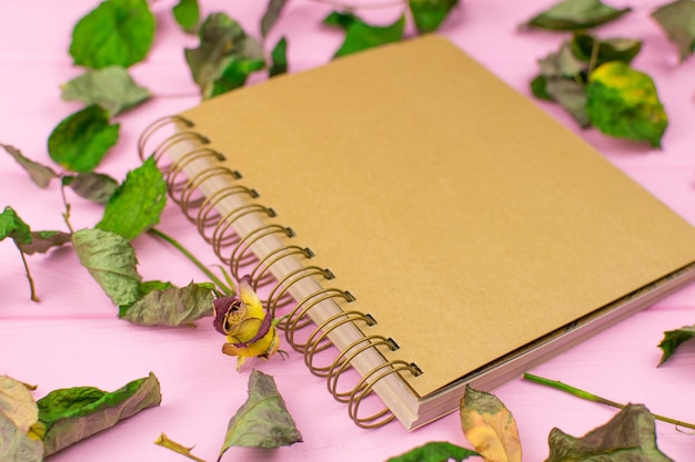 Carnet de croquis sur un fond en bois rose avec des feuilles séchées d'une rose