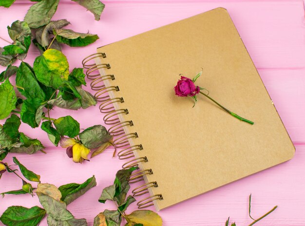 Un carnet de croquis sur un fond en bois rose avec une rose sèche