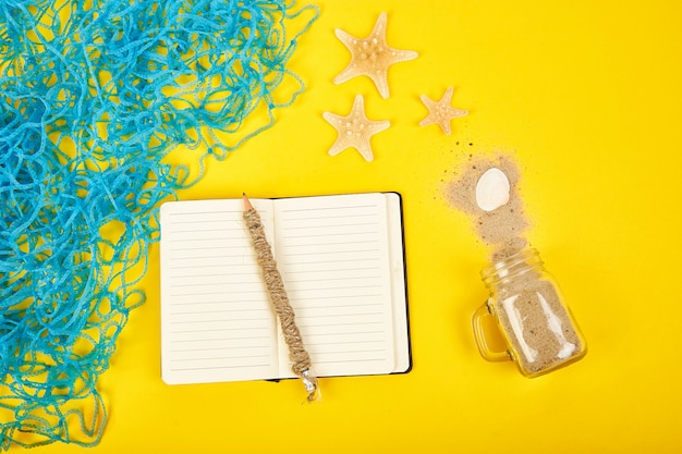 Carnet, étoiles de mer et coquillages, verre avec sable