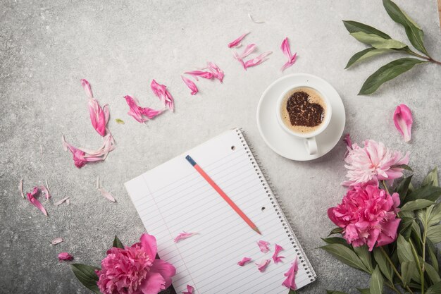 Carnet de notes, pivoines et tasse de café sur fond de béton clair avec texte juin