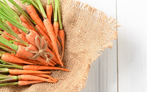 carotte fraîche, carotte bébé sur sac et fond bois blanc et vue de dessus, ce légume est une exception