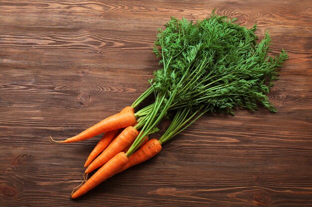 Carottes biologiques fraîches avec des sommets verts sur fond de bois