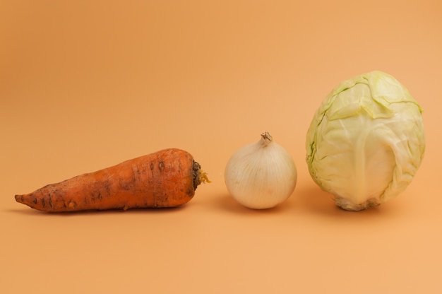 Carottes biologiques, oignons et chou sur fond beige.