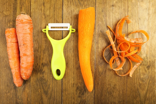 Carottes crues et éplucheuse sur table en bois