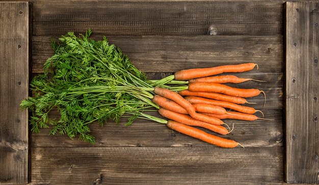 Carottes fraîches avec des feuilles vertes sur fond en bois. Concept d'aliments biologiques