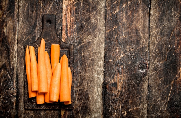 Carottes fraîches pelées sur une planche à découper sur la vieille table en bois