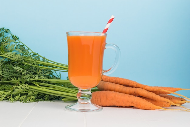 Carottes fraîches et un verre avec un smoothie et un tube à cocktail sur fond bleu.