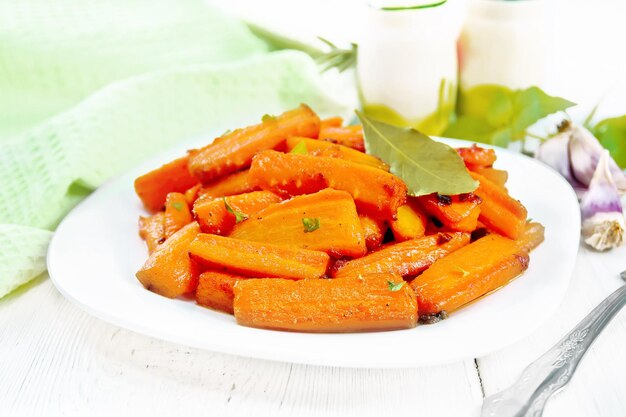 Carottes frites avec des épices de feuille de laurier à l'ail et des oignons verts dans une assiette de basilic et une serviette sur fond de planche de bois clair