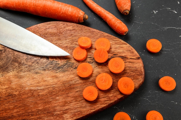 Carottes sur hachoir en bois et planche de travail noire, certaines d'entre elles coupées en cercles avec un couteau de chef, vue d'en haut