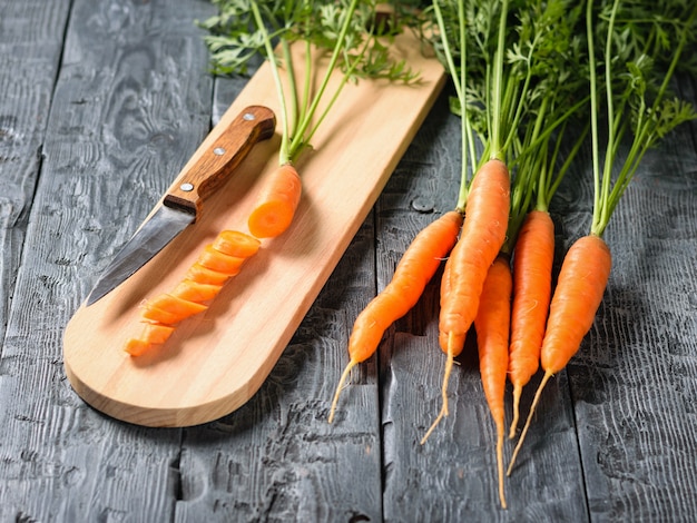 Carottes en tranches avec un couteau sur la planche à découper sur la table en bois foncé.