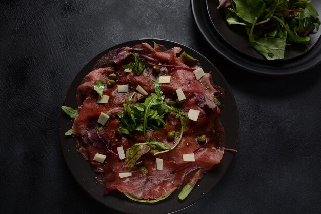 Carpaccio de boeuf au parmesan, câpres et roquette. Avec de l'huile d'olive et de la sauce soja