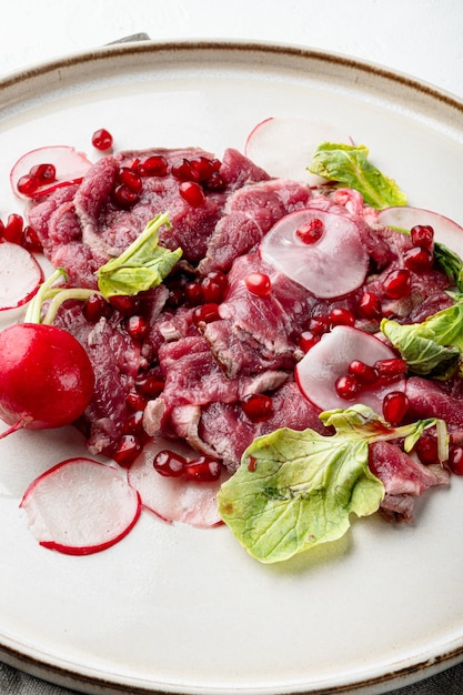 Carpaccio de boeuf classique, avec radis et grenat, sur assiette, sur pierre blanche