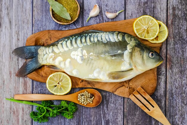 Carpe miroir sur une planche à découper entourée de légumes. Poisson frais avant la cuisson. Poissons et légumes.