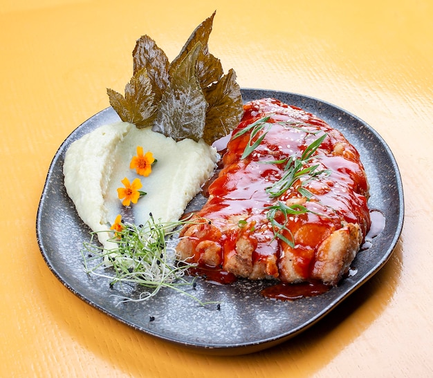 Carpe en sauce chinoise aigre-douce avec purée de pommes de terre et feuilles de vigne Sur un plateau en céramique sombre